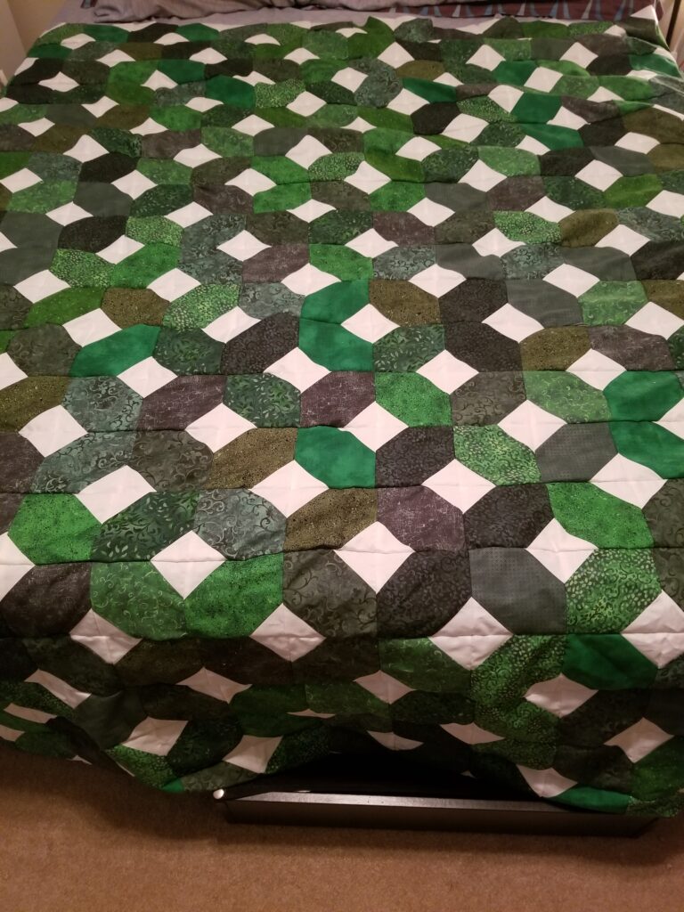 Xs and Os quilt top laid out on a bed.