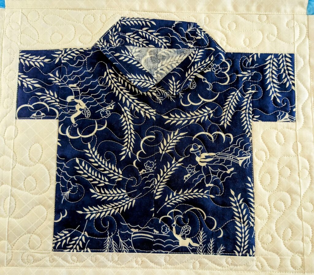 A shirt block with a loopy meander quilting in the background and waves quilted in the shirt.