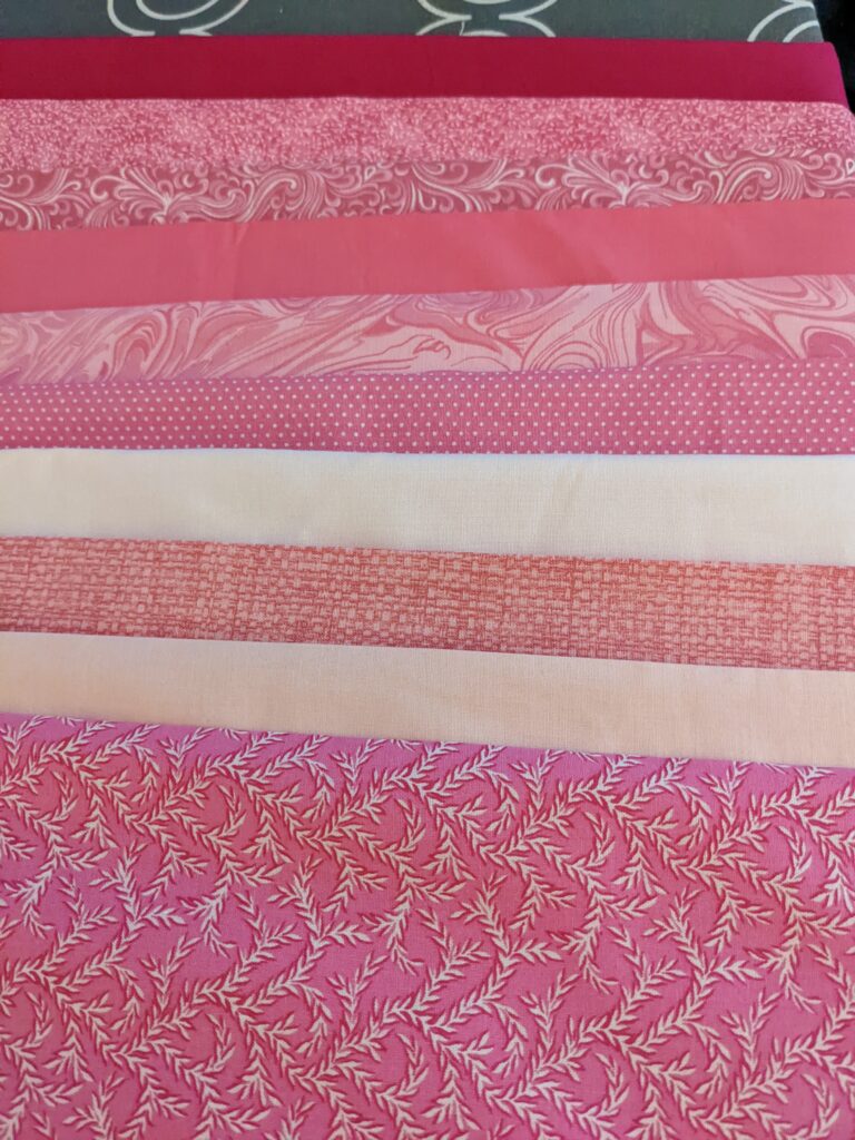 Folded fabric yardage in different hues of pink.