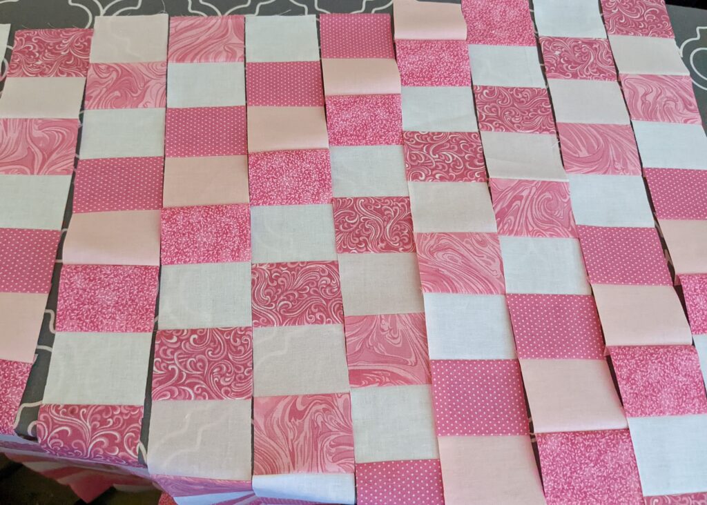 Strip set of pink fabrics that were cut into squares, laid out on my ironing board.