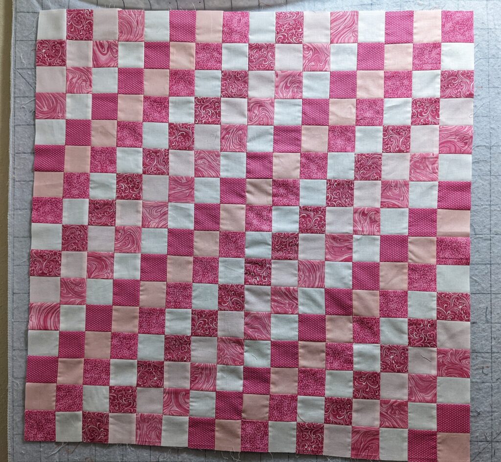 Part of the Around the World quilt in pinks laid out on my design wall after being sewn together.