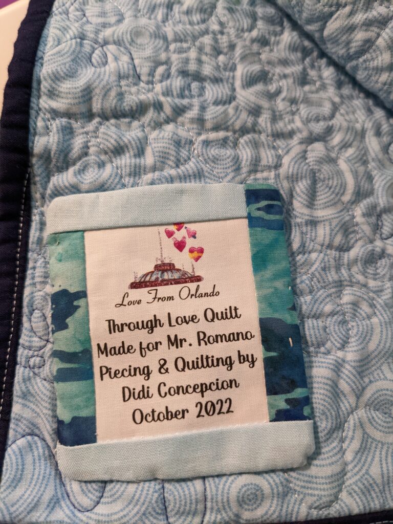 Close up of the quilt label on the back of the quilt. The label says: Through Love Quilt, Made for Mr. Romano, Piecing & Quilting by Didi Concepcion, October 2022"