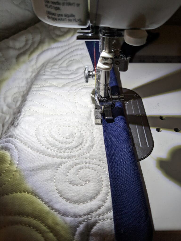 A closeup of the 1/16" compensating foot being used to machine sew the binding to the front.