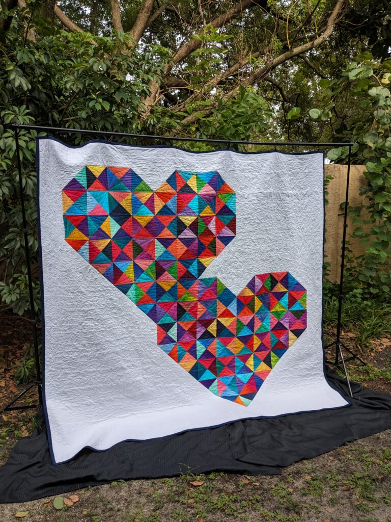 The fully completed quilt hanging from a black frame.